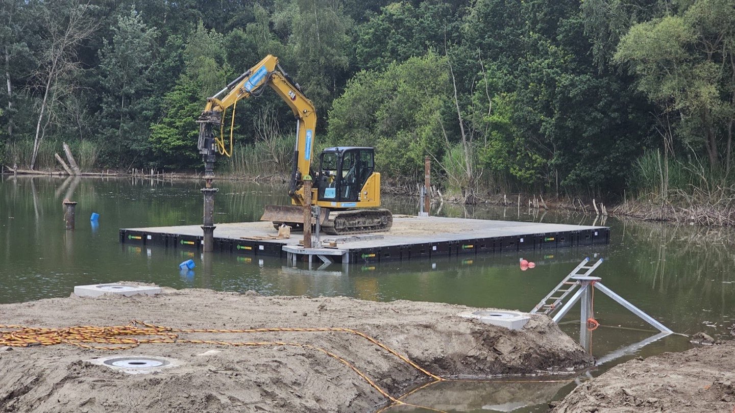 Graafkraan op een drijvend ponton plaatst schroefpalen in een vijver